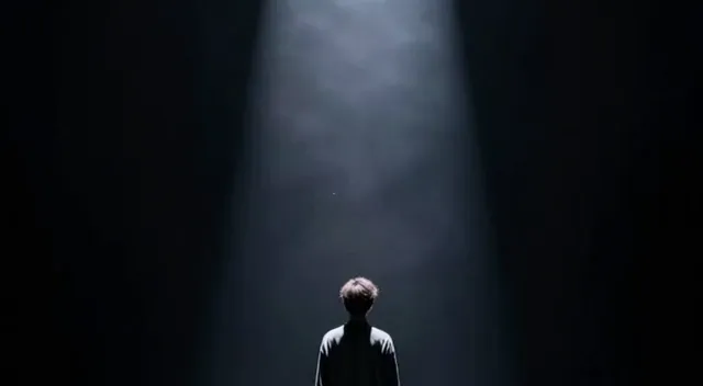 a person standing alone in darkness with a single light path ahead, symbol of choice and future, dramatic lighting…