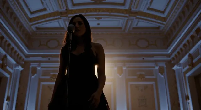 A cinematic video of a woman singing, captured in a grand, dimly lit concert hall with high ceilings and ornate golden…
